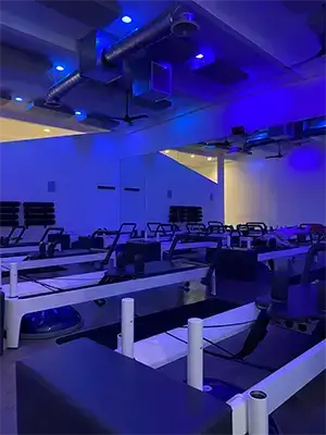 Interior view of the Avenir Pilates studio floor in Burbank, showing several reformers illuminated with dramatic blue and purple accent lighting.